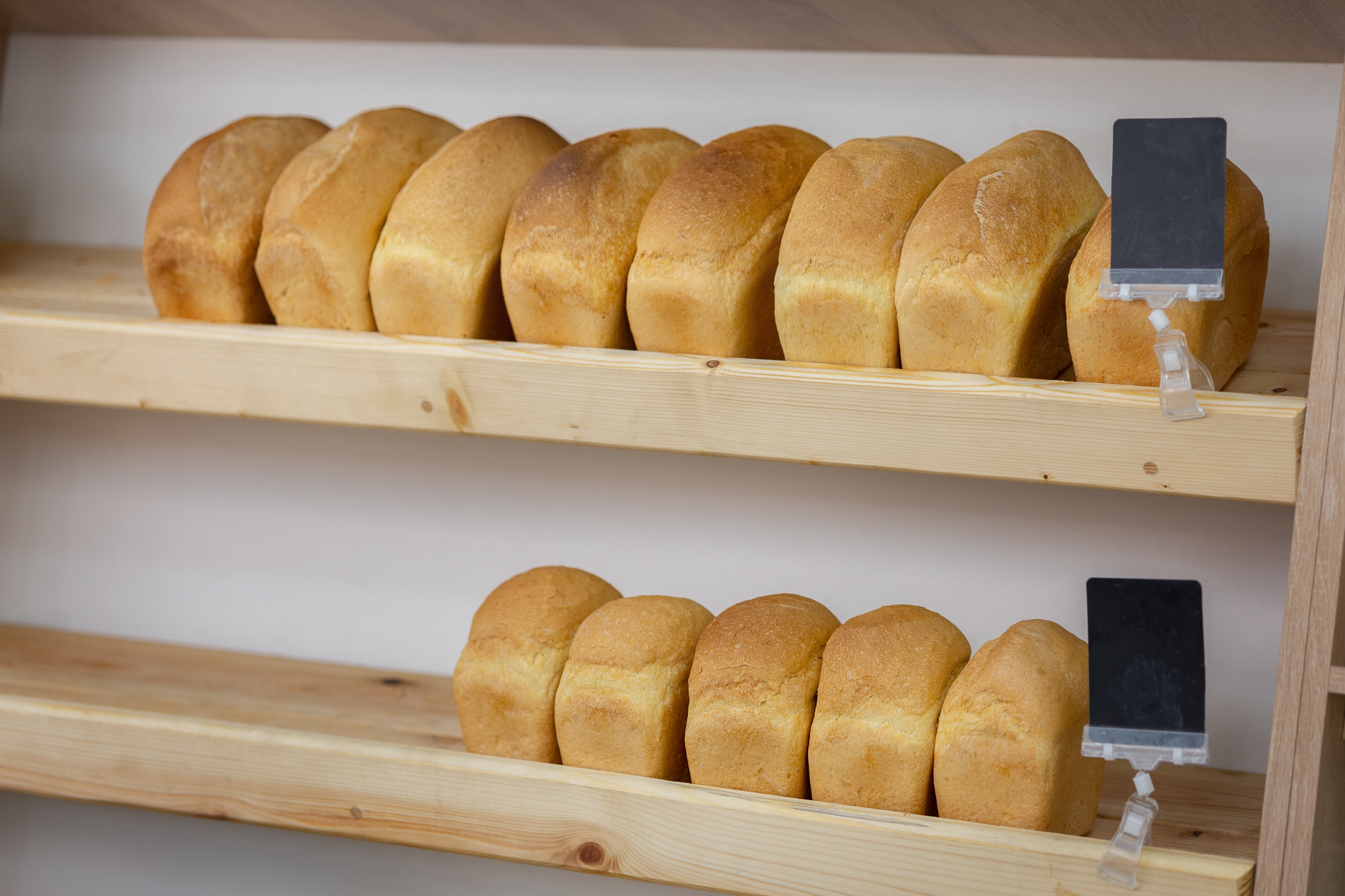 Bricks of wheat bread lie on wooden shelves in store. Fresh delicious of bread loaves in bakery, bak